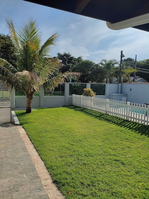 A well-maintained grassy area with a white picket fence, a palm tree, and a paved walkway. - House with Pool in Bombinhas (Bombinhas)