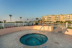 A pool area with a hot tub, lounge chairs, and a building with balconies in the background. - Enjoy Endless Views  at Beachfront Condominium! (St. Simons Island)