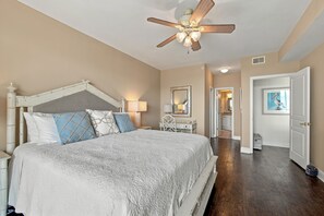 A bedroom with a bed, a ceiling fan, a nightstand, a dresser, a mirror, and a door leading to a bathroom. - Enjoy Endless Views  at Beachfront Condominium! (St. Simons Island)