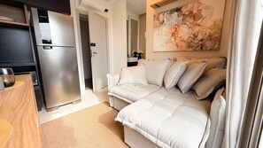 A compact living space with a kitchenette, a sofa, and a painting on the wall. - ASA Cosmopolitan 1707 Pool Blumenau (Blumenau)