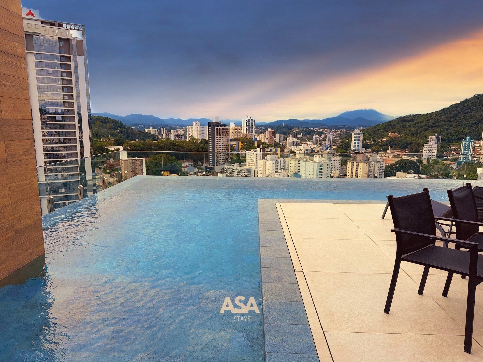 Una piscina infinita en la azotea con vistas a la ciudad, un edificio de madera a la izquierda y un letrero de ASA STAYS.