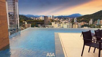 Una piscina infinita en la azotea con vistas a la ciudad, un edificio de madera a la izquierda y un letrero de ASA STAYS.