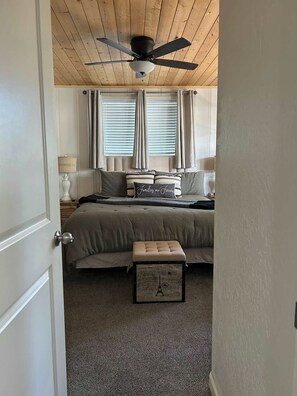 A bedroom with a bed, a ceiling fan, a window with blinds, and a small table with a suitcase. - Paradise Cove - Lake View, Dock, Near Yosemite (Bass Lake)