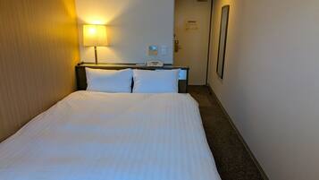 A hotel room with a bed, a bedside lamp, a phone, and a door leading to another room.