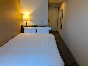 A hotel room with a bed, a bedside lamp, a phone, and a door leading to another room. - Smile Hotel Kagoshima-chuo Ekimae (Kagoshima/Nishida)
