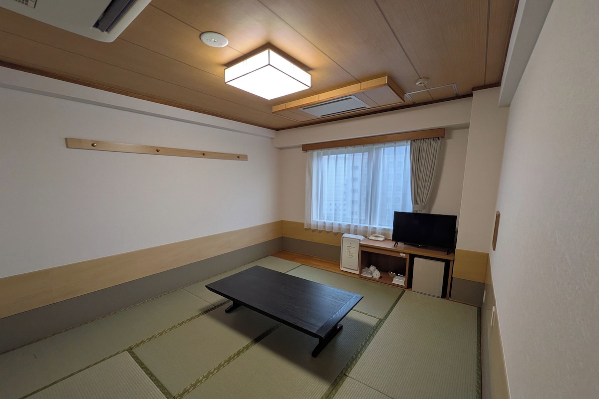 A room with tatami flooring, a television on a wooden stand, and a ceiling light fixture.