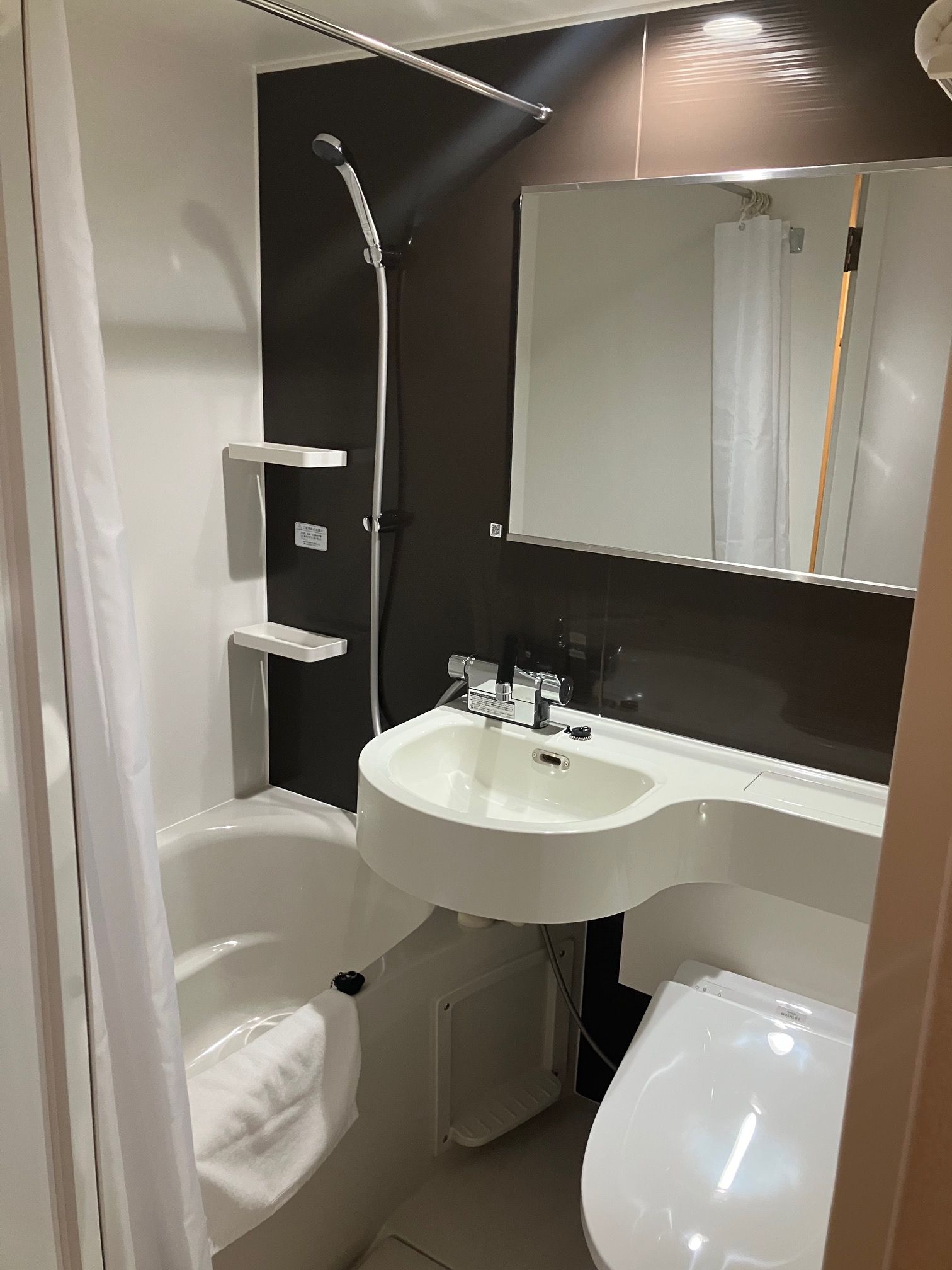 A compact bathroom with a white sink, a mirror, a shower, and a toilet.