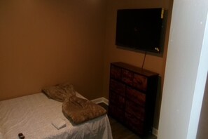 Una habitación con una cama, un televisor montado en la pared y un aparador de madera.