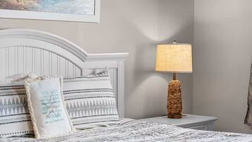 A neatly made bed with patterned bedding, a bedside lamp with a woven base, and a wall-mounted painting.