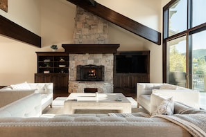 A living room with a stone fireplace, wooden beams, and a large window offering a view. - 4BR Park Meadows townhome with mountain views, sleeps 10 (Park City)
