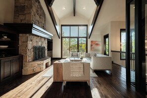 A spacious living room with a stone fireplace, wooden flooring, and large windows offering a view of the outdoors. - 4BR Park Meadows townhome with mountain views, sleeps 10 (Park City)