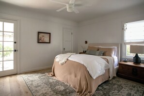 A bedroom with a bed, a nightstand, a ceiling fan, a window with blinds, and a door. - Casa Mika - Designer Curated 2BR/1BA Retreat Near SoFi, Intuit Dome & The Forum (Los Angeles)