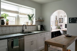 A kitchen with a window, a sink, cabinets, a wooden table, and a coffee machine. - Casa Mika - Designer Curated 2BR/1BA Retreat Near SoFi, Intuit Dome & The Forum (Los Angeles)