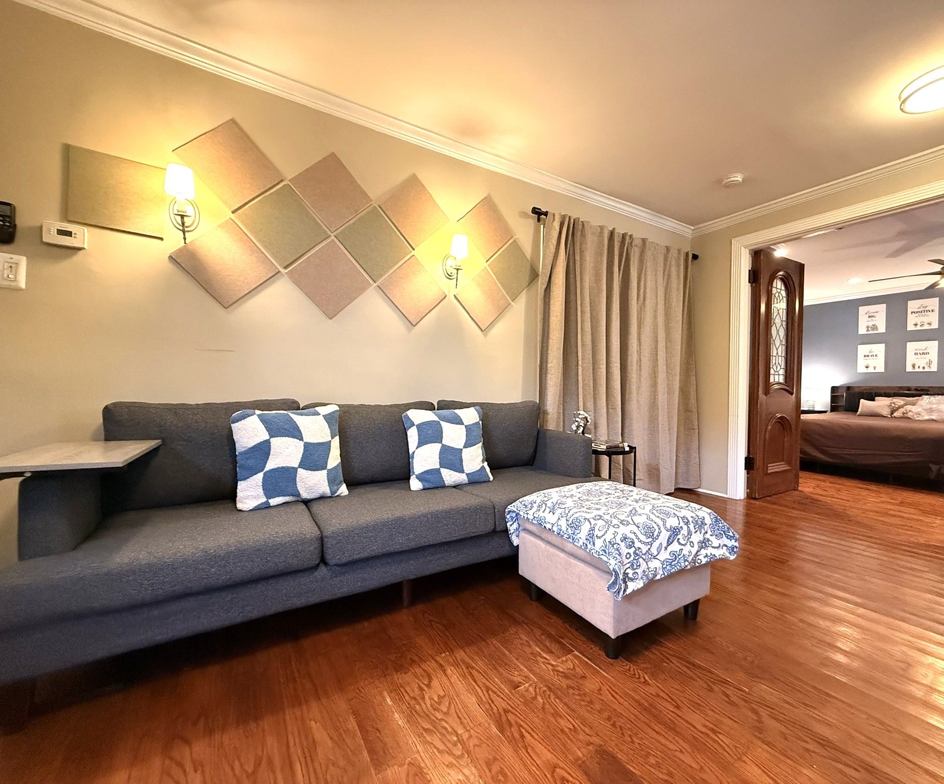 A modern living room with a grey sofa, patterned cushions, a small side table, and a wooden floor.