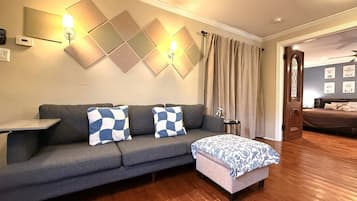 A modern living room with a grey sofa, patterned cushions, a small side table, and a wooden floor.