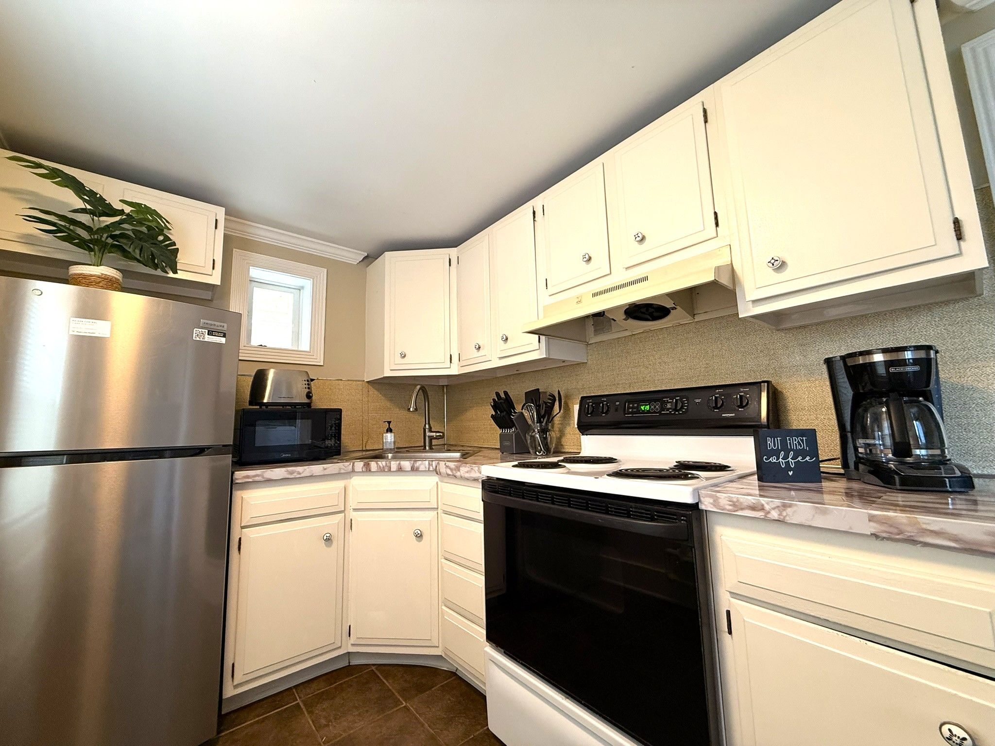 A kitchen with white cabinets, a stainless steel refrigerator, a microwave, a stove, and a coffee maker.