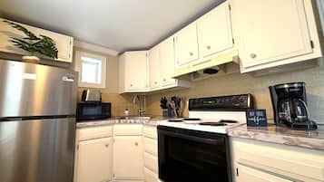 A kitchen with white cabinets, a stainless steel refrigerator, a microwave, a stove, and a coffee maker.