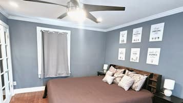 A bedroom with a bed, a ceiling fan, a window with a curtain, and motivational wall art.