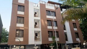 Edificio residencial de varios pisos con balcones, unidades de aire acondicionado y acceso mediante portón.