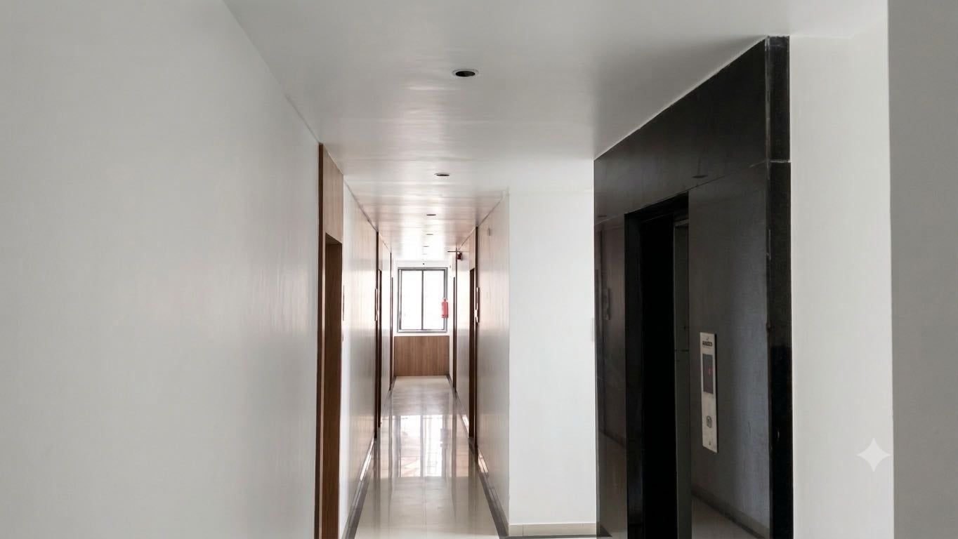 Un pasillo con una puerta a la derecha, un detector de incendios en la distancia e iluminación empotrada en el techo.