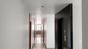 Un pasillo con una puerta a la derecha, un detector de incendios en la distancia e iluminación empotrada en el techo.