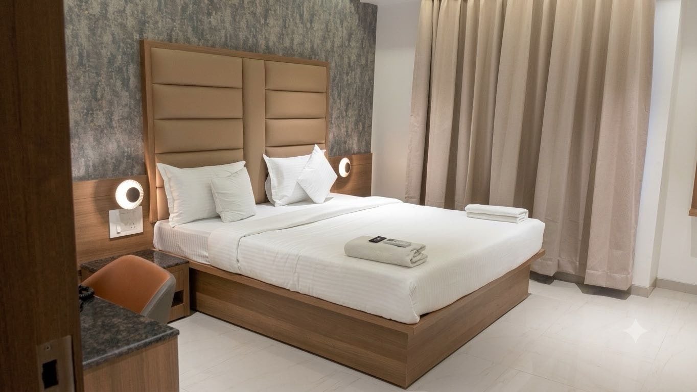 A modern hotel room with a wooden bed frame, white bedding, and a bedside table with a lamp.