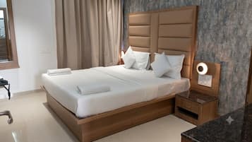 Una cama bien hecha con cabecera de madera, una mesita de noche con lámpara y un baño con espejo y toallero.