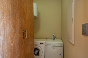 A laundry room with a washing machine, dryer, and ironing board. - La Marina | 2BR Waterfront + Marina Views (Brakkeput)