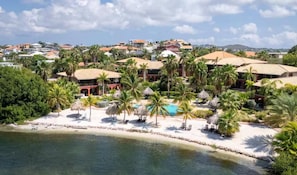 A resort with beachfront properties, palm trees, and a swimming pool. - La Marina | 2BR Waterfront + Marina Views (Brakkeput)