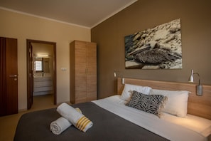 A hotel room with a bed, a large painting, a wardrobe, and a bathroom visible through an open door. - La Marina | 2BR Waterfront + Marina Views (Brakkeput)