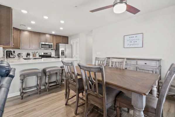 A modern kitchen with wooden cabinets, a dining table, and bar stools. - Sea Oats | 3BR Oceanfront Escape (North Myrtle Beach)