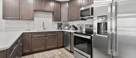 A modern kitchen with stainless steel appliances, wooden cabinets, and a marble countertop.