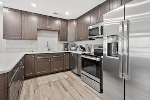A modern kitchen with stainless steel appliances, wooden cabinets, and a marble countertop. - Sea Oats | 3BR Oceanfront Escape (North Myrtle Beach)