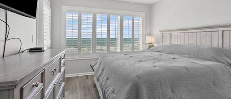 A bedroom with a large bed, a dresser, a ceiling fan, and a window with a view.