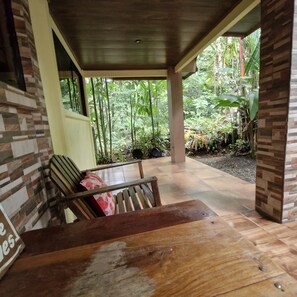 An outdoor seating area with a wooden table and benches, surrounded by a covered porch and a view of dense greenery. - Green Paradise Home. (Provincia de Alajuela)
