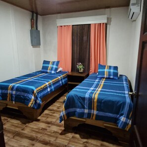 A room with two wooden beds, each with a blue and yellow plaid bedspread. There is a small table with a potted plant between the beds. - Green Paradise Home. (Provincia de Alajuela)