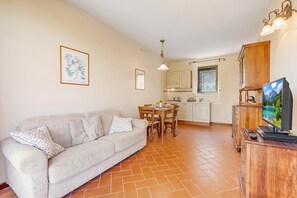 A living room with a sofa, dining table, and chairs, a kitchen with cabinets and a window, and a TV on a wooden stand. - Chianti Site Apt Fontana Shared Pool|4, Castelfiorentino, Italy (Castelfiorentino)