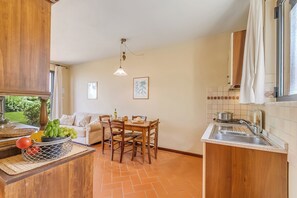A kitchen with a dining area, wooden cabinets, a tiled backsplash, and a window with curtains. - Chianti Site Apt Fontana Shared Pool|4, Castelfiorentino, Italy (Castelfiorentino)