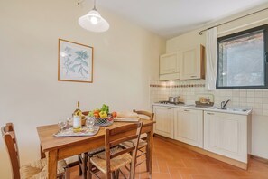 A kitchen with white cabinets, a tiled backsplash, a window with curtains, and a dining table set with food and drink. - Chianti Site Apt Fontana Shared Pool|4, Castelfiorentino, Italy (Castelfiorentino)