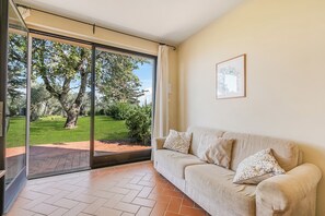 A room with a sliding glass door leading to a garden, a beige sofa with patterned cushions, and a framed picture on the wall. - Chianti Site Apt Fontana Shared Pool|4, Castelfiorentino, Italy (Castelfiorentino)