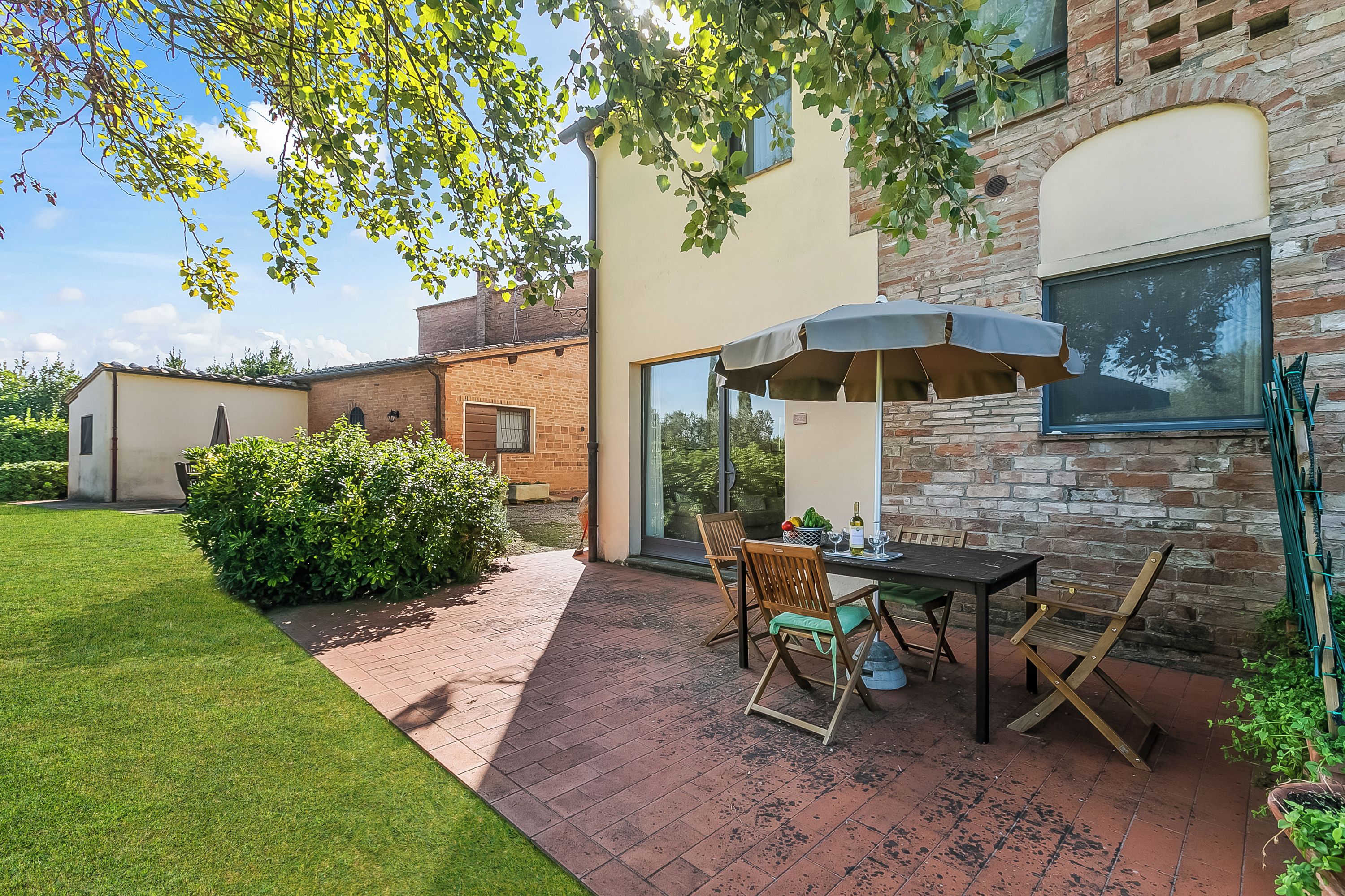An outdoor patio with a table and chairs, a brick wall, and a window.