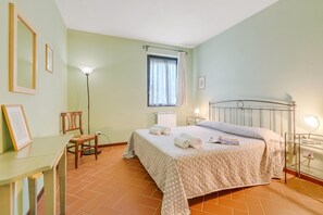 A bedroom with a bed, a desk, a chair, a floor lamp, and a window with curtains. - Chianti Site Apt Prato Shared Pool| 4, Castelfiorentino, Italy (Castelfiorentino)