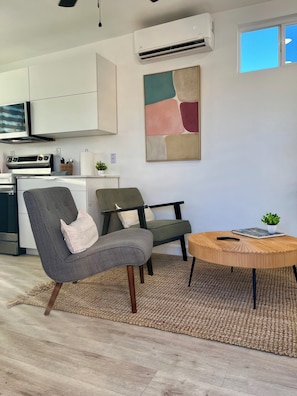 A modern living room with a sofa, chairs, a coffee table, and a kitchen in the background. - LUUM House (Phoenix)