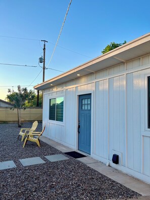 A single-story building with a blue door, a window, and a chair outside. - LUUM House (Phoenix)