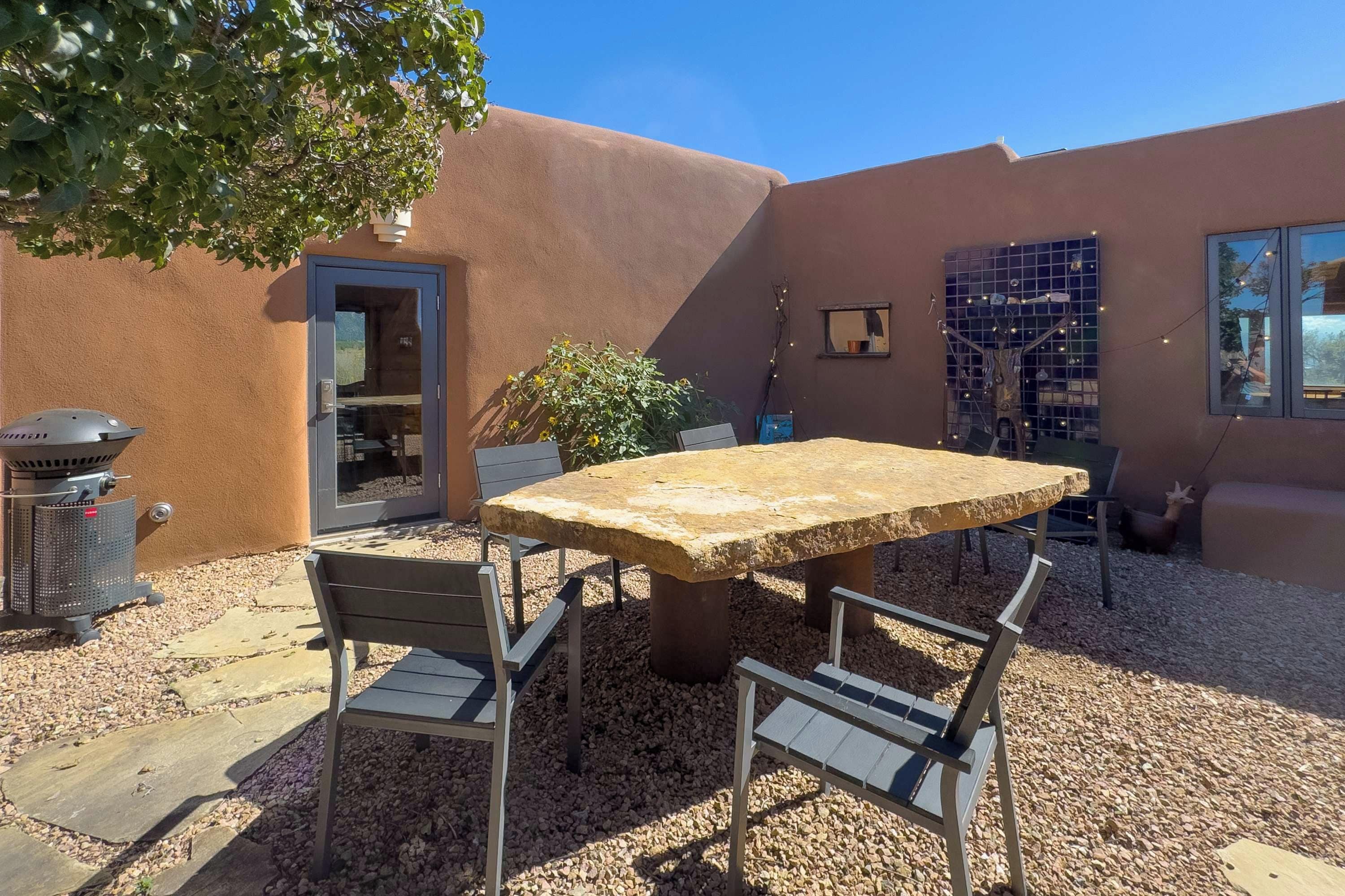 Un patio exterior con una mesa y sillas de piedra, una parrilla y un pequeño jardín.