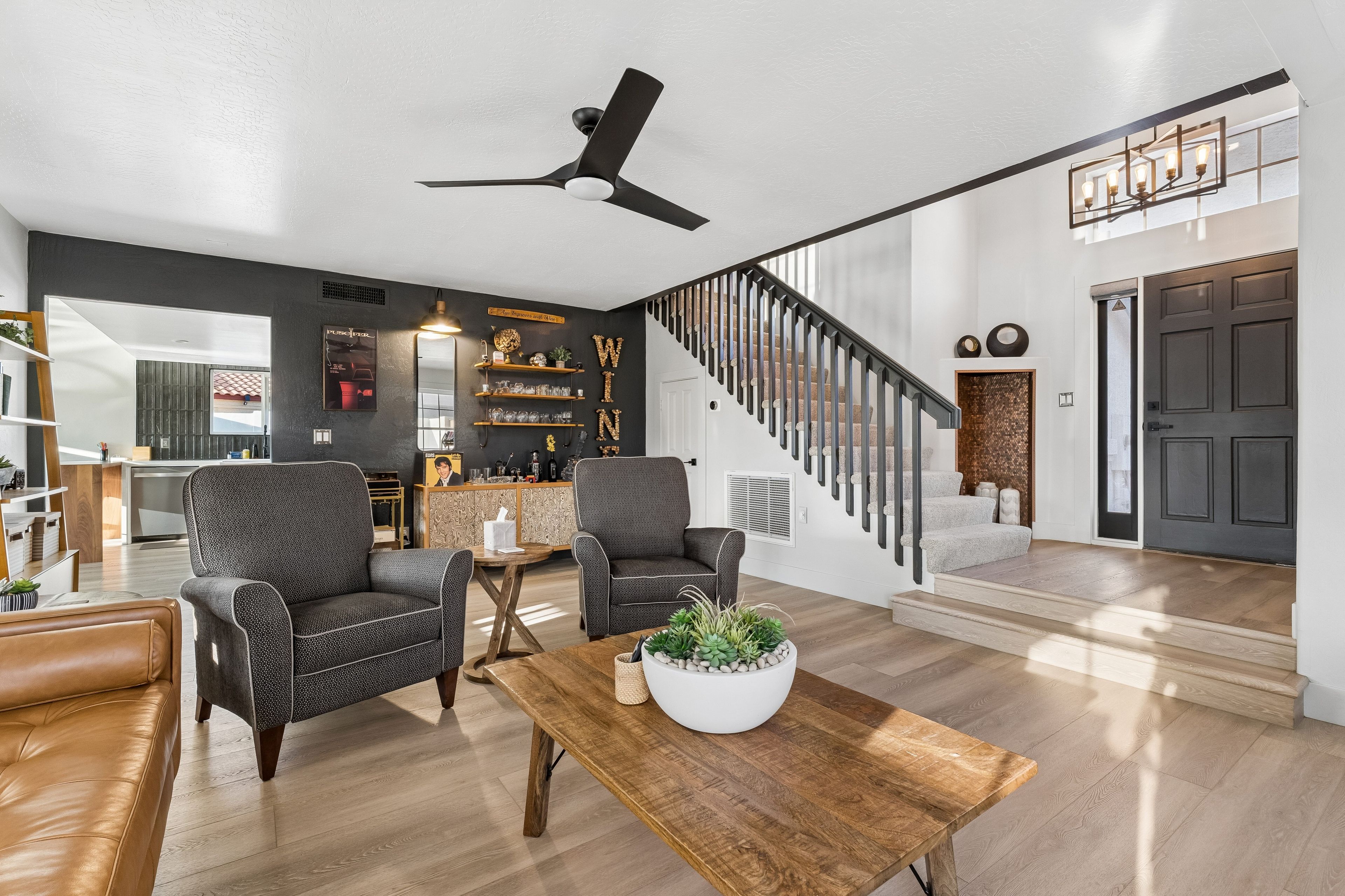 A modern living room with a staircase, leather sofas, a coffee table, and a ceiling fan.