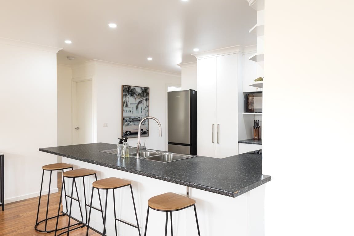 A modern kitchen with a central island, bar stools, a stainless steel refrigerator, and white cabinetry.