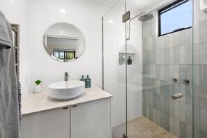A modern bathroom with a round mirror, a white sink, and a glass shower enclosure. - Renovated on Elizabeth (Anglesea)