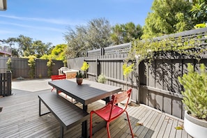 An outdoor patio with a wooden deck, a table, and red chairs. - Renovated on Elizabeth (Anglesea)