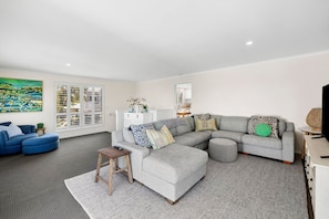 A modern living room with a grey sectional sofa, a blue armchair, and a small wooden stool. - Renovated on Elizabeth (Anglesea)
